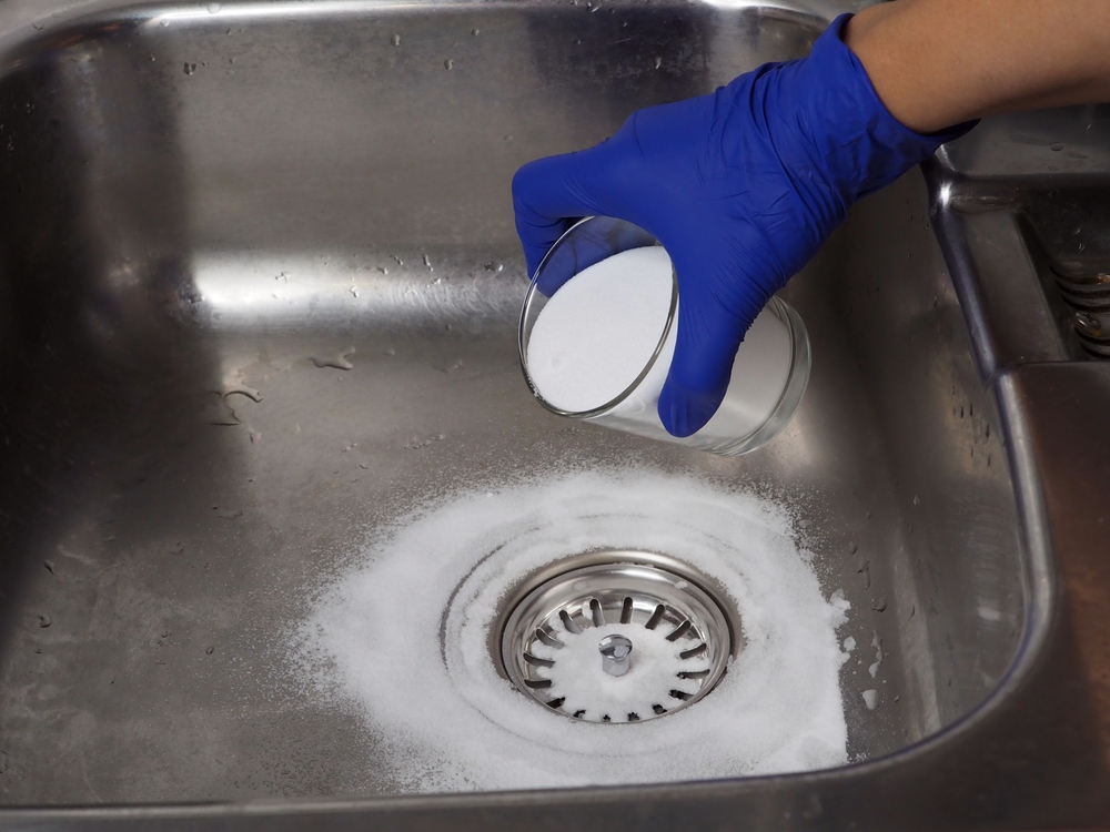 gloved hand cleaning drain with baking soda