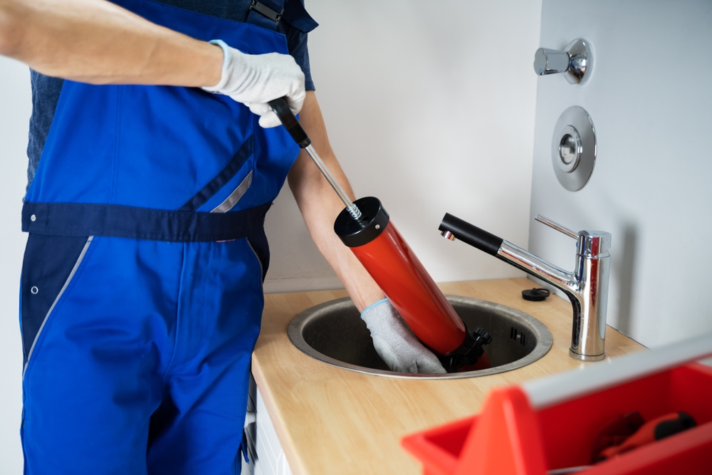 a plumber with a blue hat working under a sink